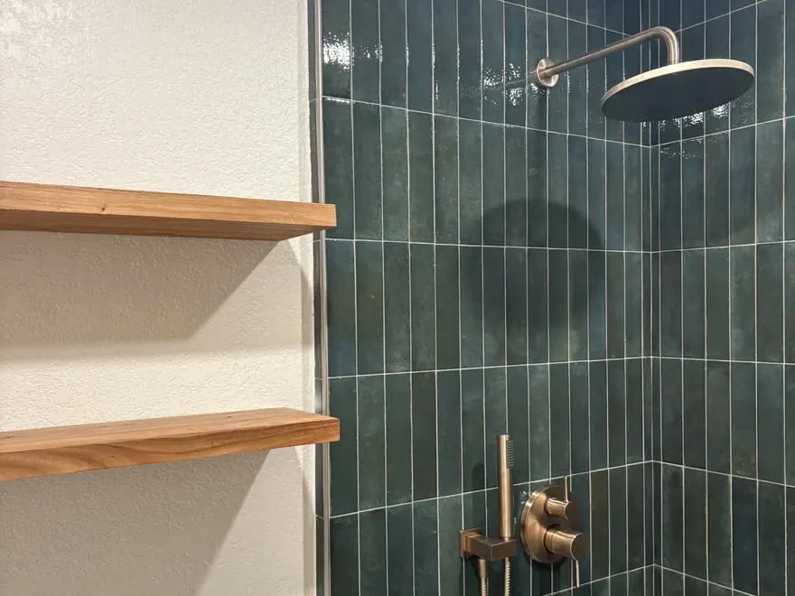 Green tile shower with brass fixtures and floating shelves